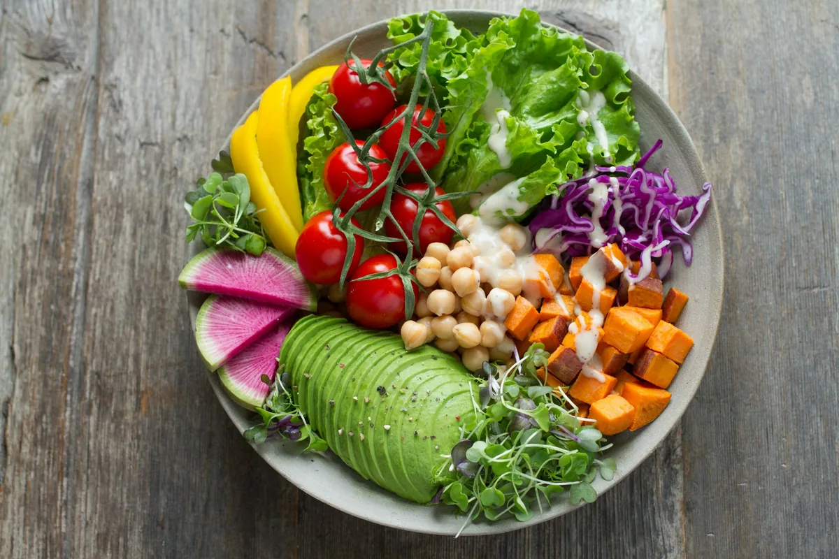 A bowl of leafy greens, chickpeas, avocado, tomatoes, and roasted sweet potato.