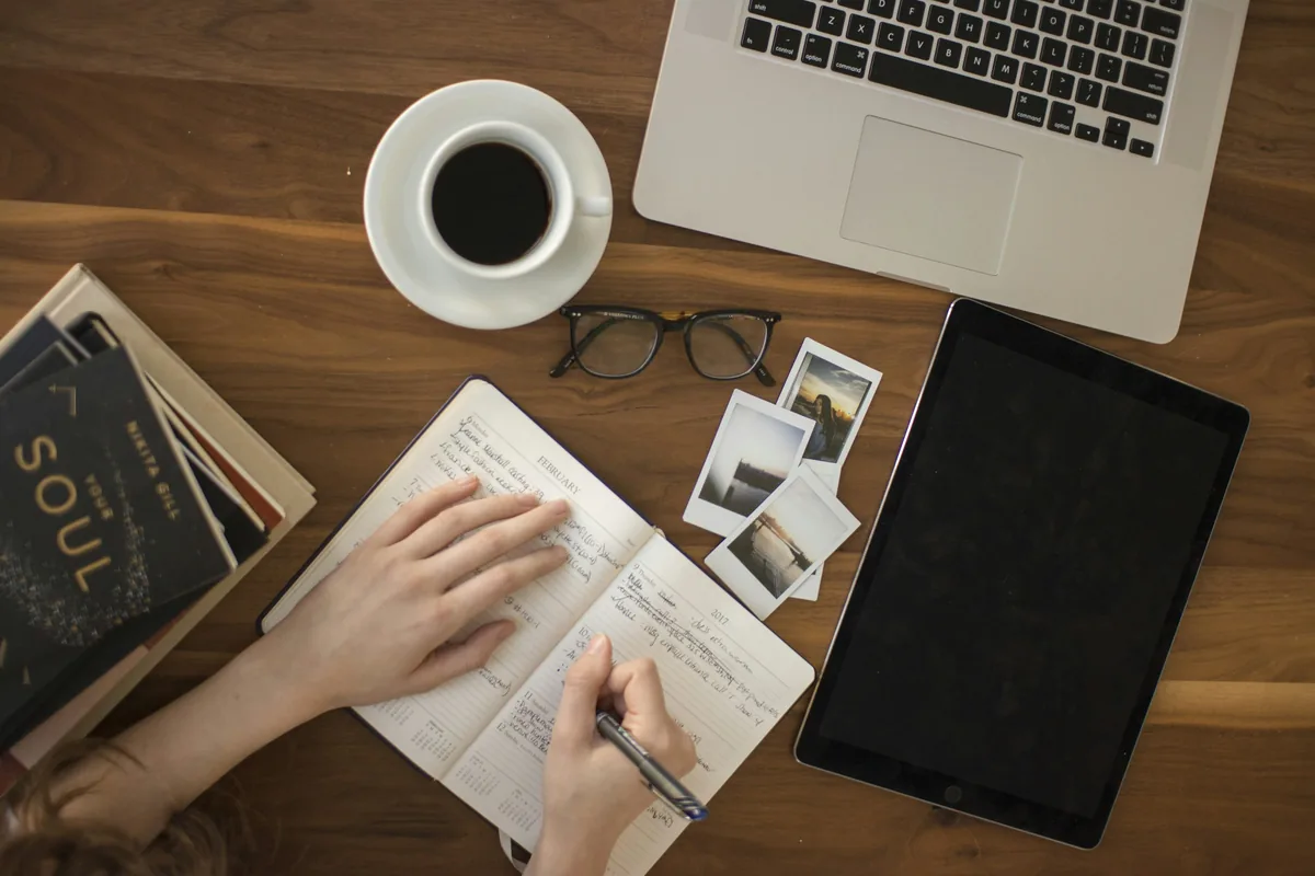 A hand holds a ballpoint pen while writing notes in an open notebook.